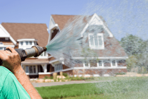 Man wearing green shirt hydroseeds a lawn of a beautiful house