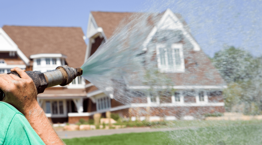 Man wearing green shirt hydroseeds a lawn of a beautiful house